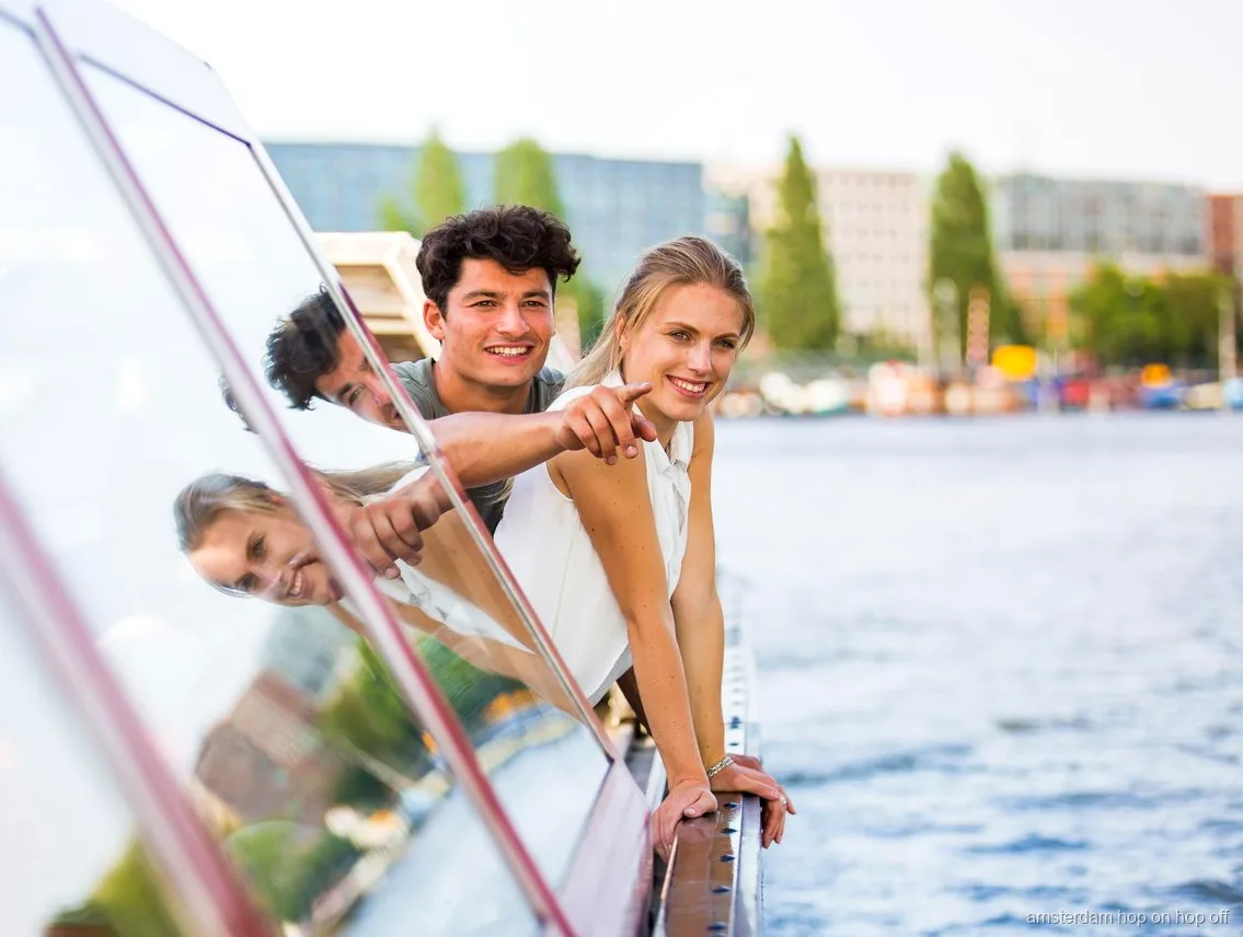 Pasajeros en el barco turístico hop-on hop-off de Amsterdam junto a casas de canal históricas