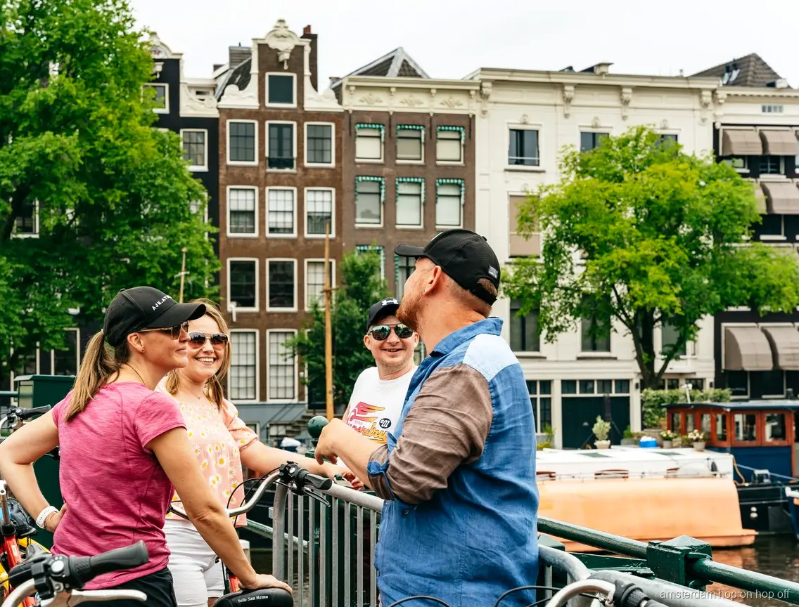 Cyclistes du Big Bike Tour passant devant une maison de canal historique d'Amsterdam
