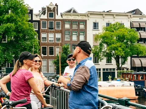 Ciclistas del tour en bicicleta de Amsterdam pasando junto a una casa de canal histórica